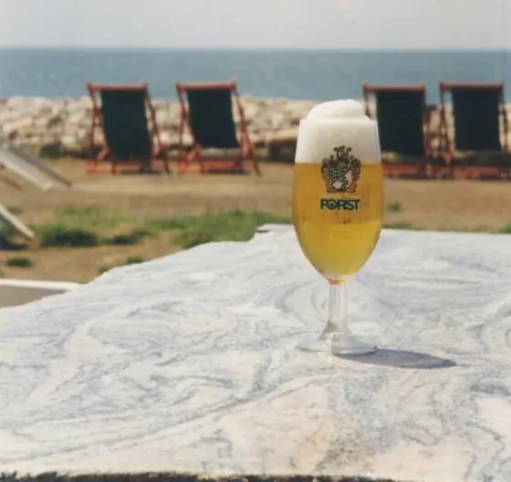 Un bicchiere di birra Forst su un tavolo di marmo, con il mare e le sdraio sullo sfondo.