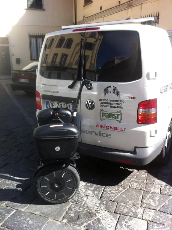 Il furgone bianco di Tutto Spina parcheggiato su una strada lastricata del centro, con un monopattino elettrico accanto.