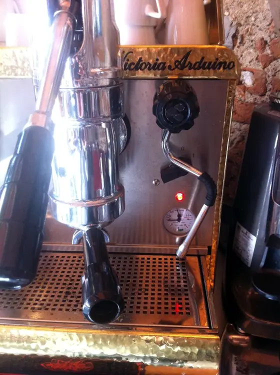 Una macchina per espresso Victoria Arduino in ottone e acciaio cromato, con la leva e il manometro.